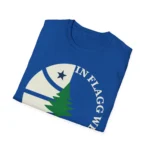 Folded royal blue t-shirt showing the “IN FLAGG WE TRUST” logo and pine tree print.
